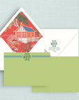 A stationery set featuring a white envelope with return address on flap and a red chinoiserie lining, a two-sided green notecard with monogram lettering on front, all arranged on a pale blue textured background.