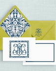 A stationery set featuring a two-sided note card in white with a navy blue ornate two-letter monogram and border and simple border on the reverse side, a matching bright green envelope with a blue and white floral patterned liner and return address with monogram on the flap.