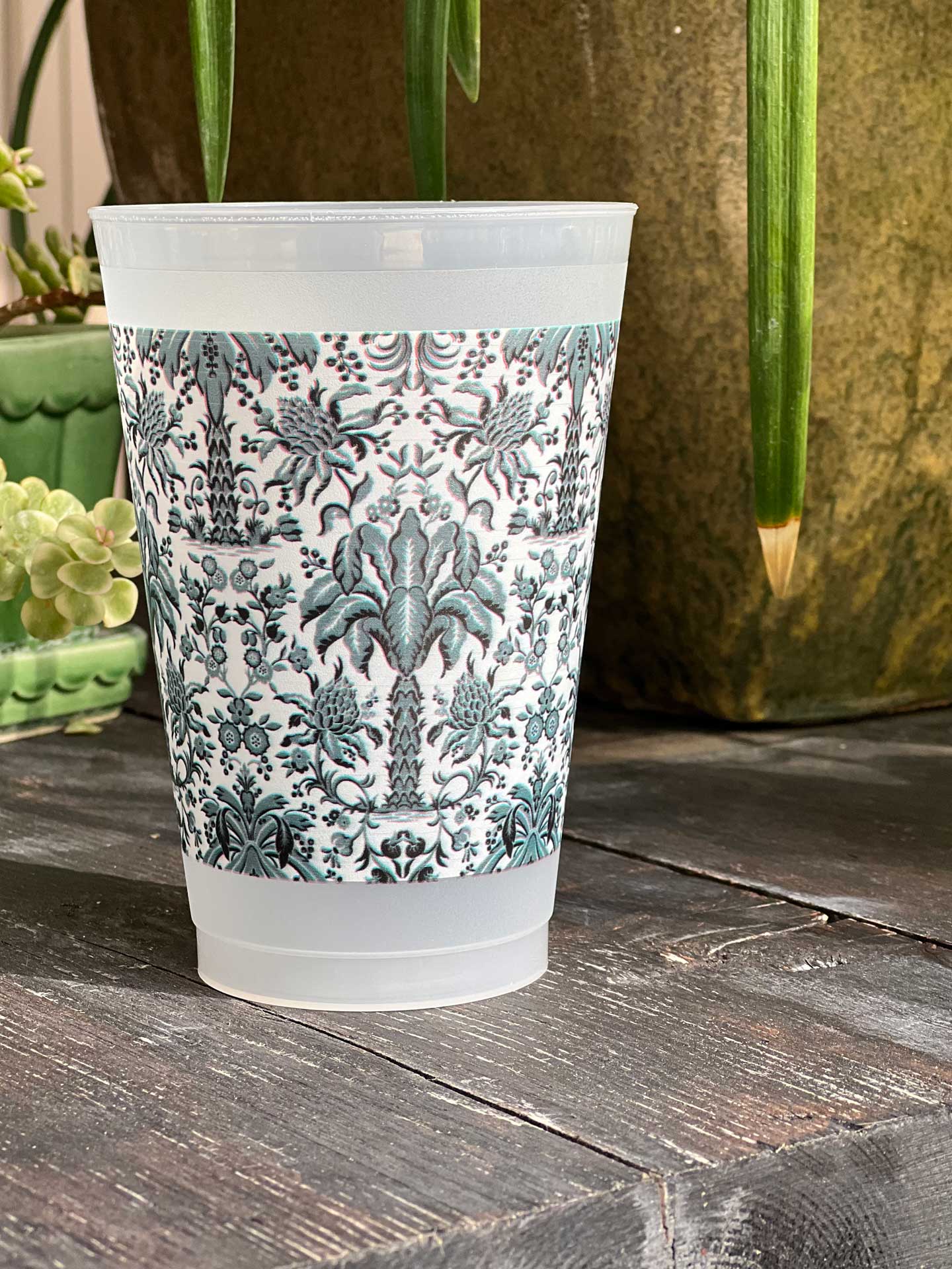 A clear frosted plastic cup with a blue and white floral damask palm tree pattern full wrap.