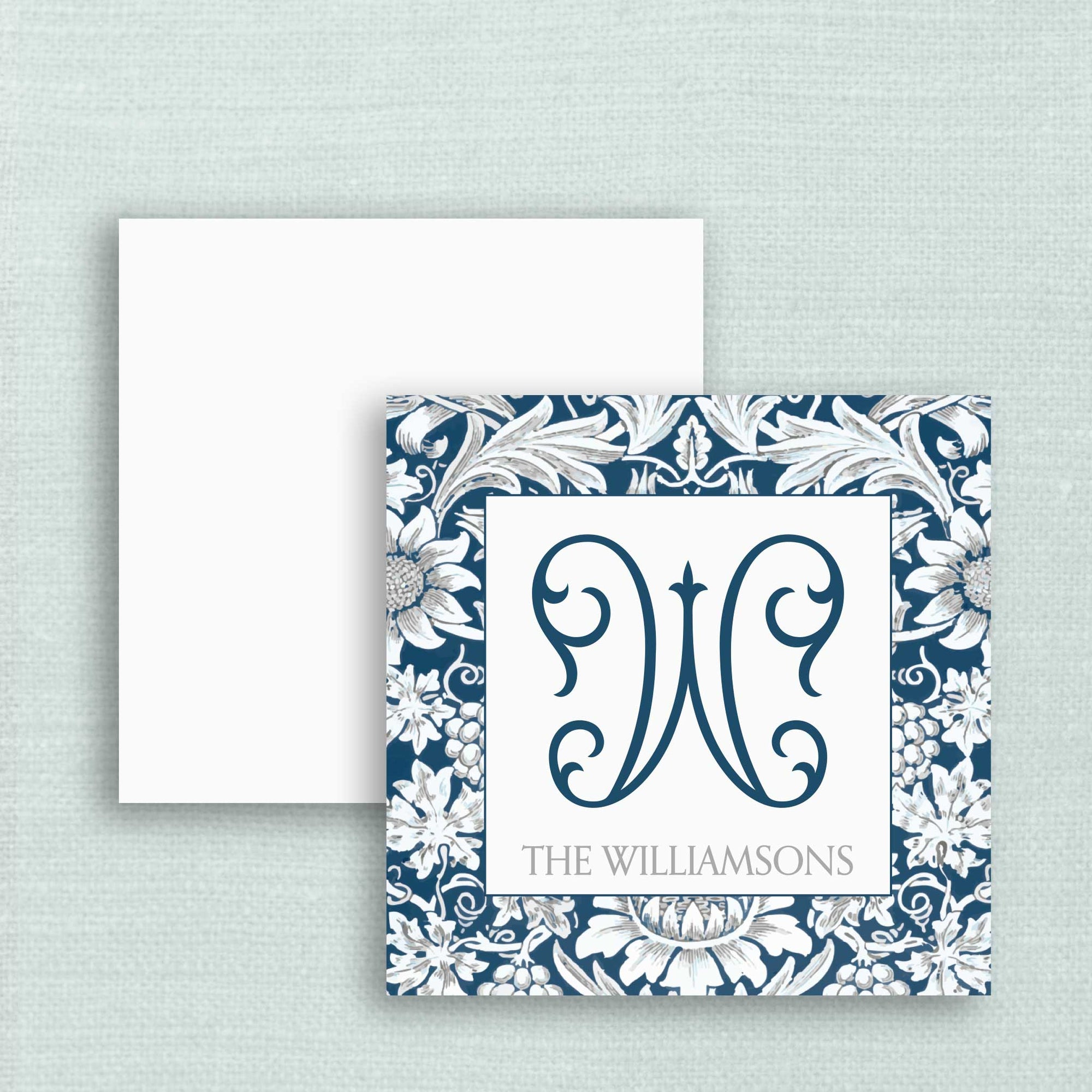 A square gift tag with a blue and white damask floral border and a large ornate monogram in the center on the front side with the last name below, shown with a white reverse side.