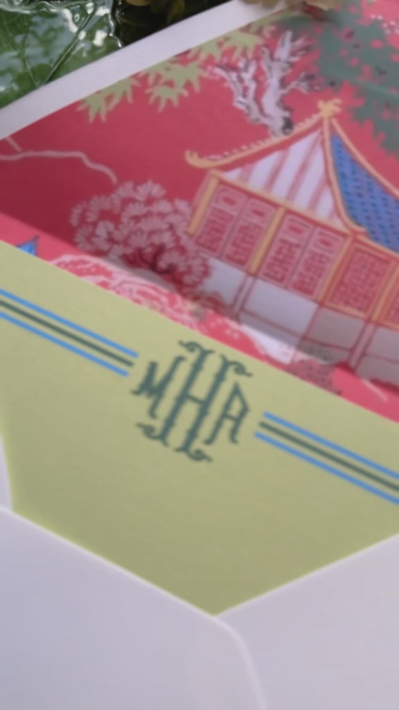 Video showing stationery set that includes a green notecard with monogram on front and a white envelop with return address on the flap and a red chinoserie print lining that features a pagoda design.